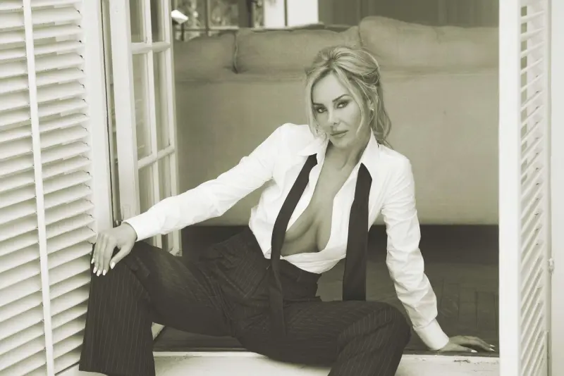 Black-and-white portrait of Katherine Taylor seated on a windowsill in a white shirt, suspenders, and pinstripe trousers