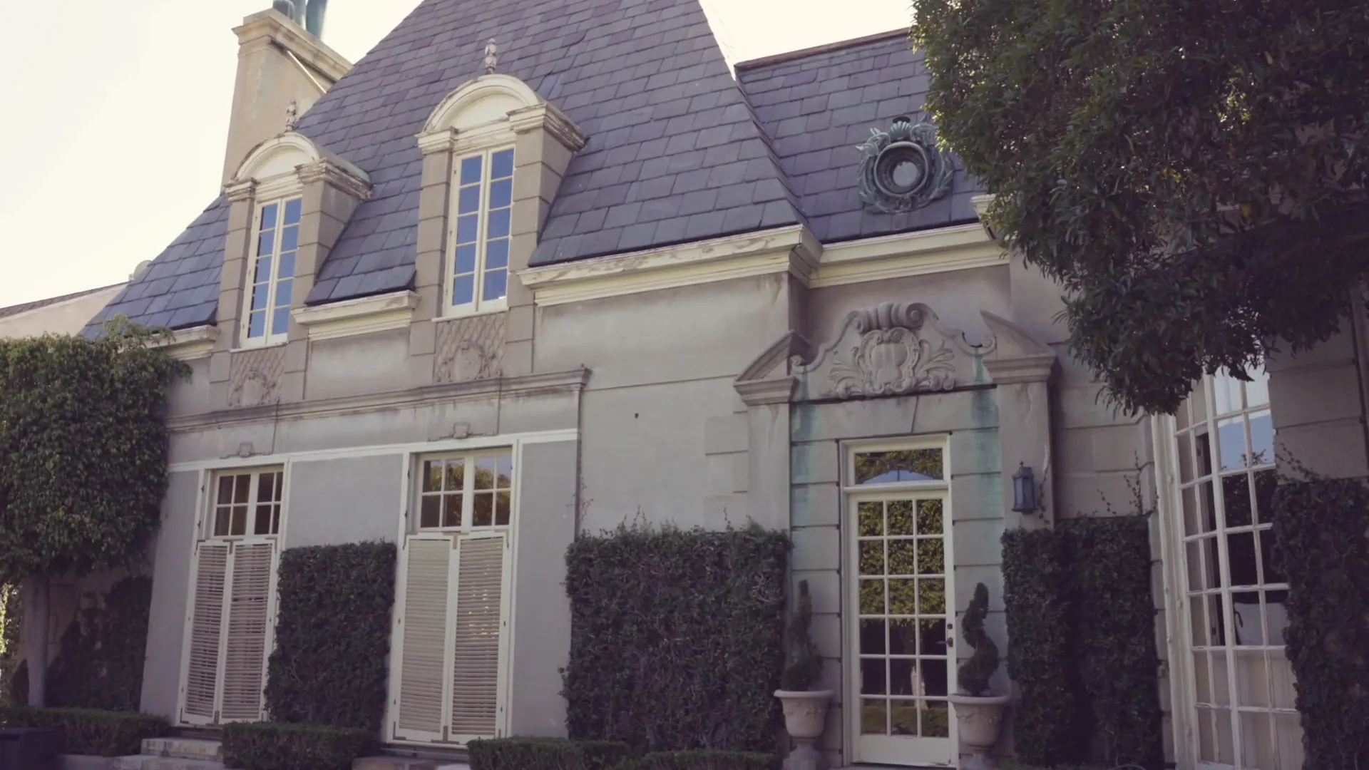 Stone house with a slate roof, clipped hedges, and a white glass-paned door